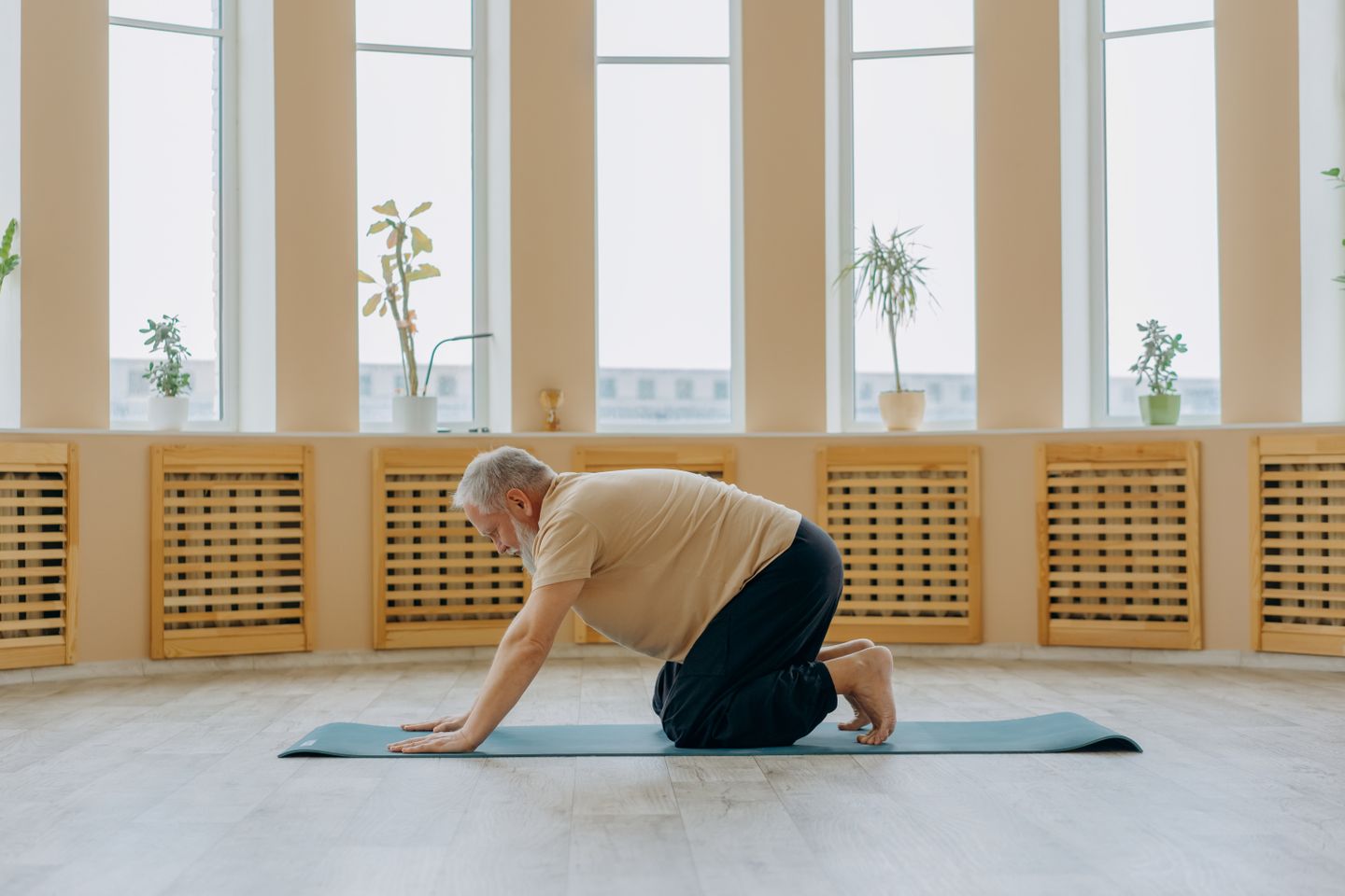 Elderly man kneeling on a yoga mat in a serene indoor setting for mindfulness and health.